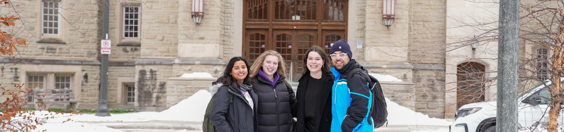 Four students in the snow stand outside an academic building.