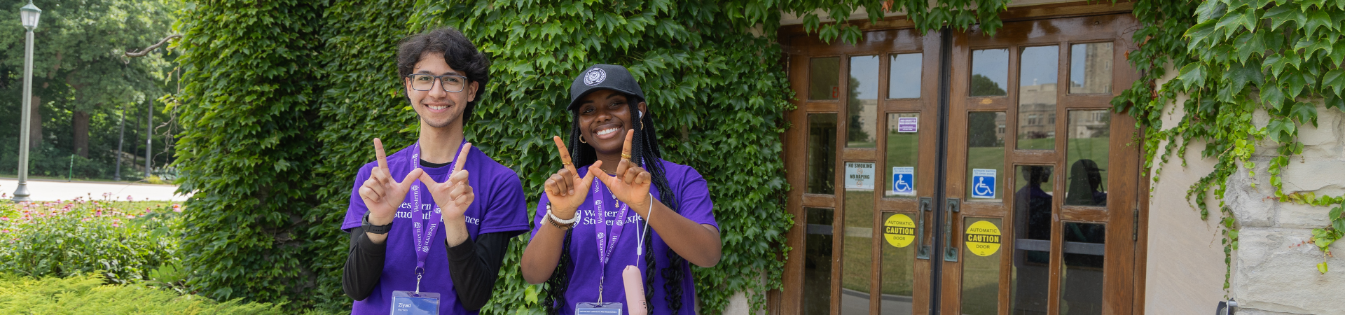 Two students dressed in purple hold up a W sign with their hands