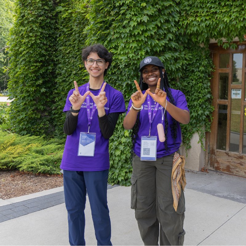 Two students dressed in purple hold up a W sign with their hands