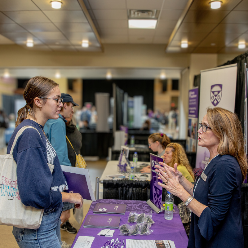 A student engages with a older lady at an event booth.