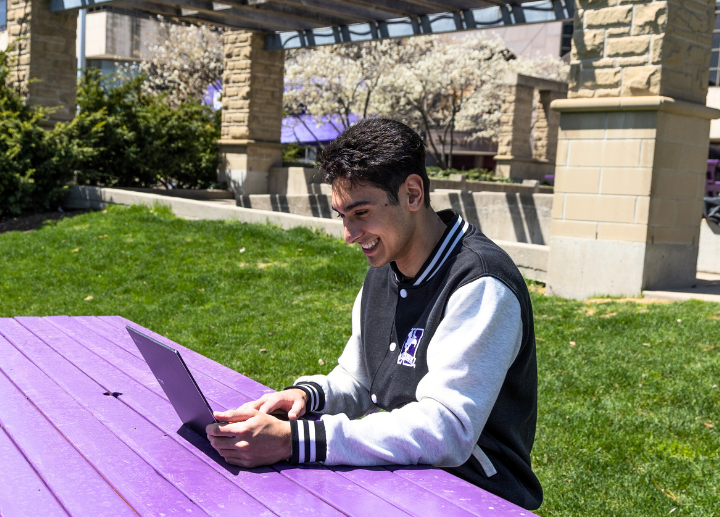A young man sits outside using a laptop.