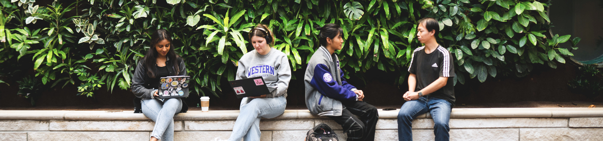 Four students sit in front of a plant wall.