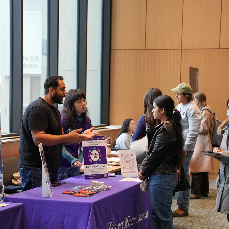 Several students listen to a speaker at an event booth.